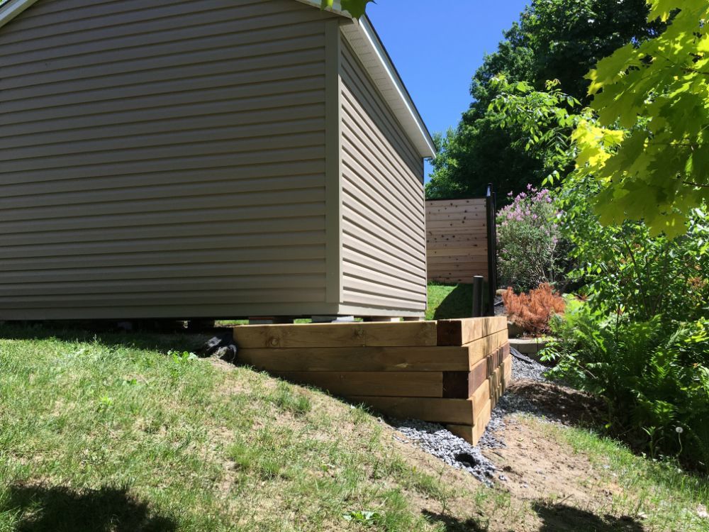 Mur de soutènement en bois soutenant une structure sur une colline herbeuse.