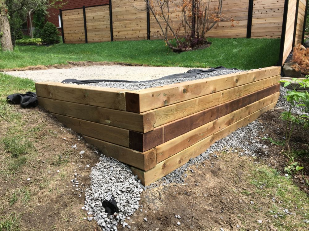 Jardinière surélevée en bois, de forme triangulaire, avec base en gravier, installée à l'extérieur.