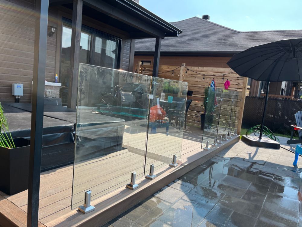 Garde-corps en verre sur une terrasse avec patio et parasol. La lumière du soleil se reflète sur la surface mouillée.