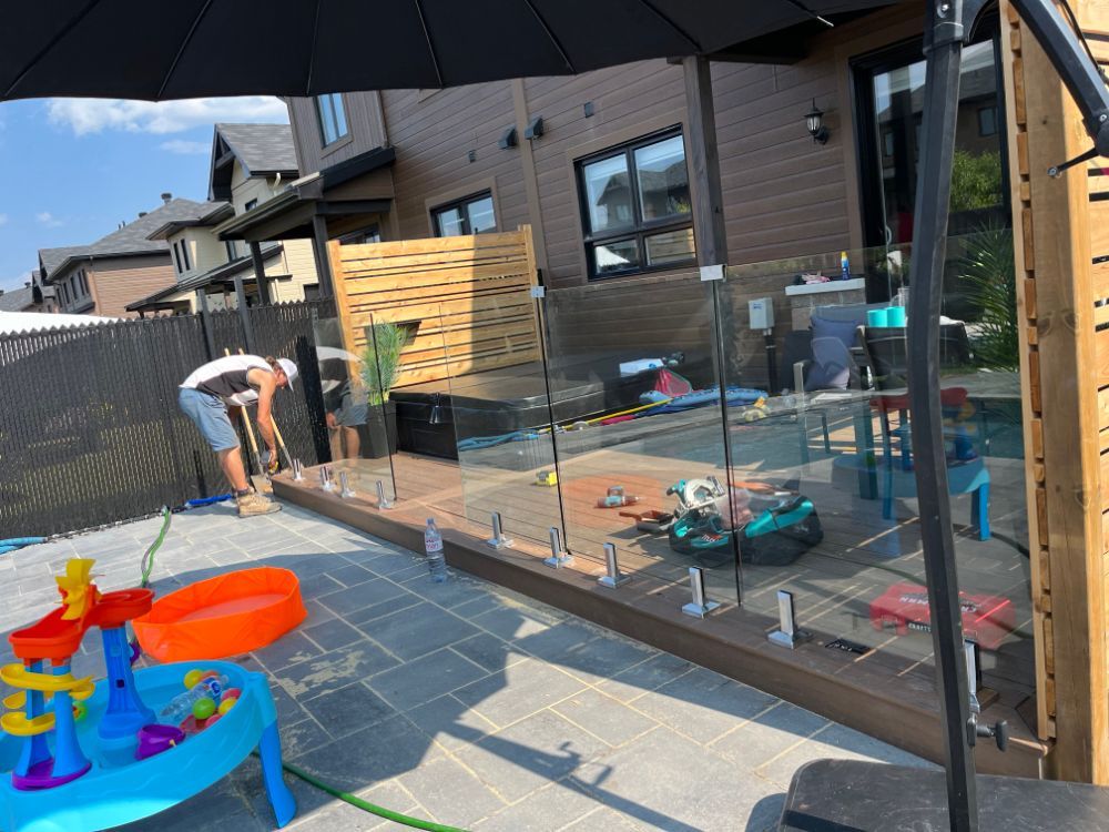 Un homme installe une clôture en verre sur un patio avec des jouets pour enfants, dans un jardin.