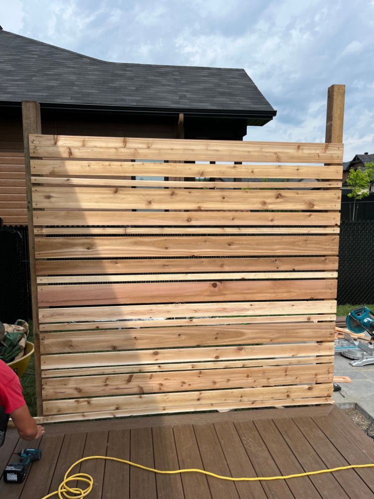 Clôture d'intimité en bois en cours de construction à l'extérieur sur une terrasse, avec une personne au travail.