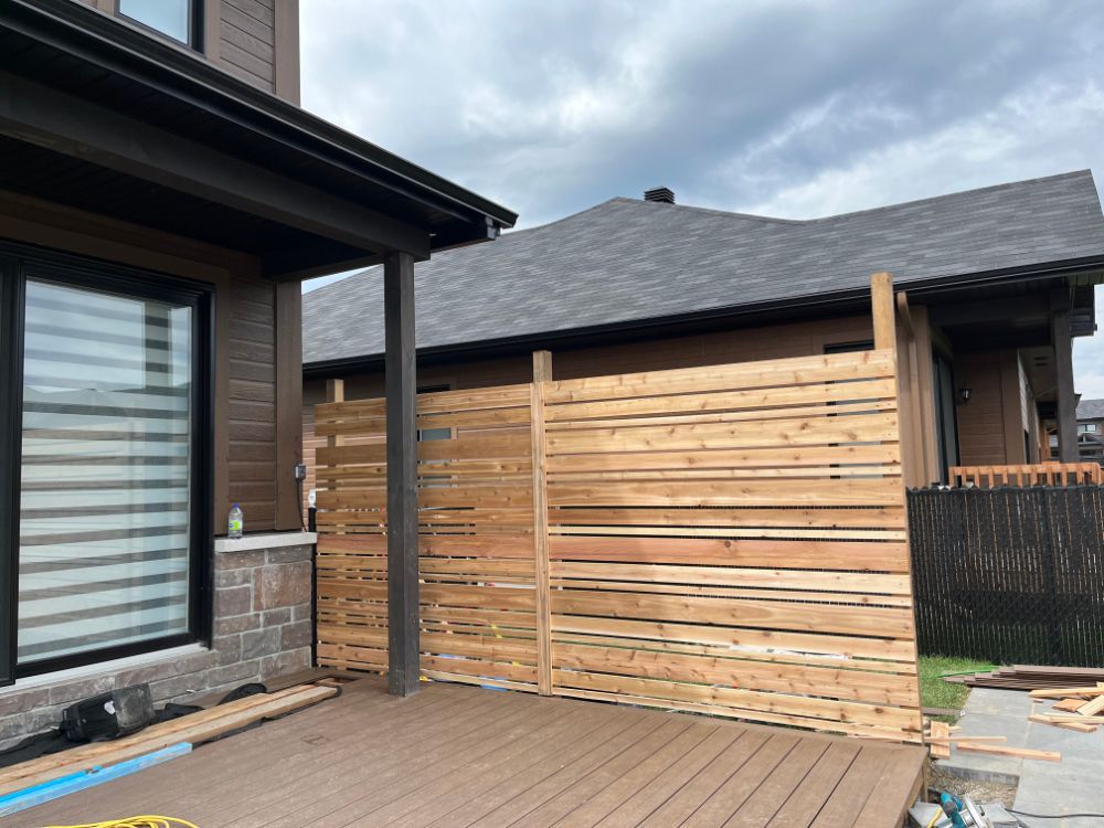 Clôture d'intimité en bois attachée à une maison avec une terrasse, sous un ciel nuageux.