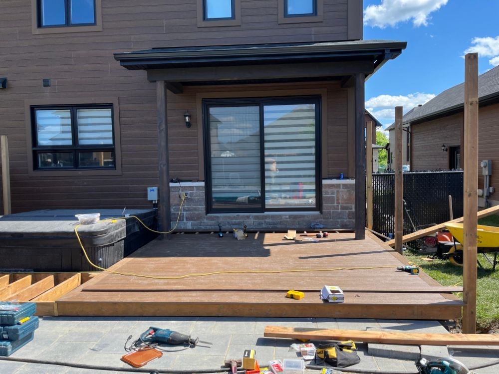 Une terrasse en bois partiellement construite à l'extérieur d'une maison aux façades brunes avec une porte coulissante en verre.