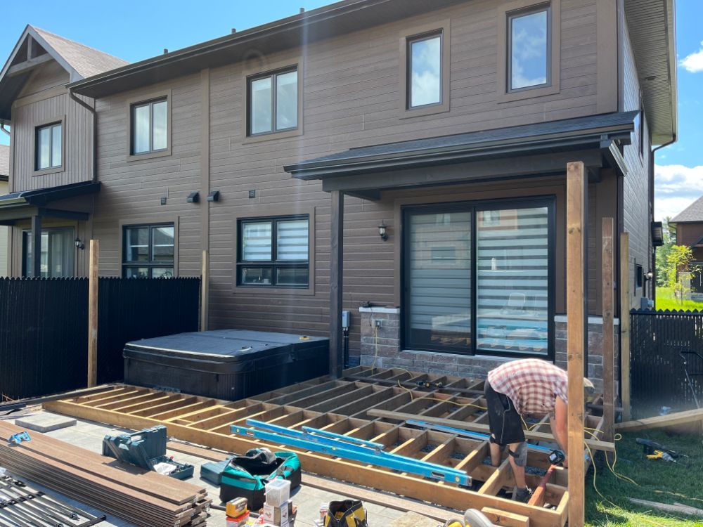 Construction d'une terrasse en bois à côté d'une maison avec jacuzzi. Un ouvrier installe les planches.