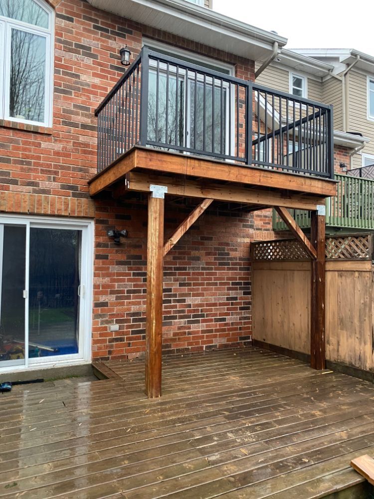 Une terrasse en bois avec une petite terrasse supérieure attachée à une maison en briques, soutenue par des poteaux.