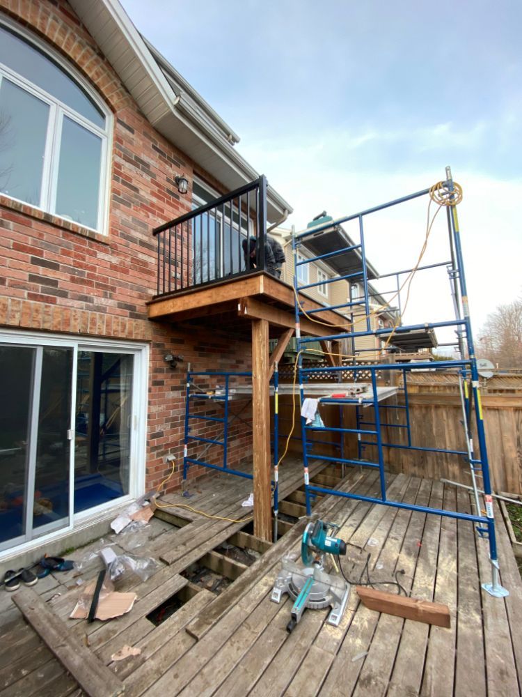 Construction d'une terrasse : ouvriers sur un échafaudage, près d'une maison en briques avec un petit balcon. Outils et matériaux visibles.