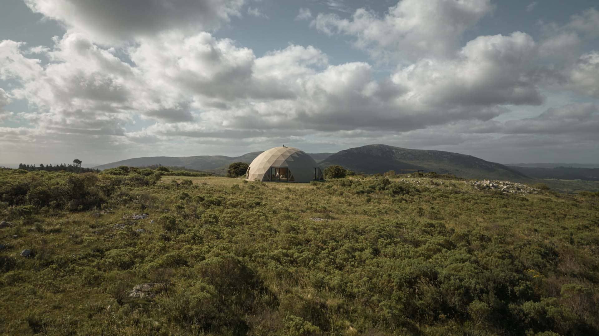 Una cúpula se encuentra en medio de un campo de hierba con montañas al fondo.