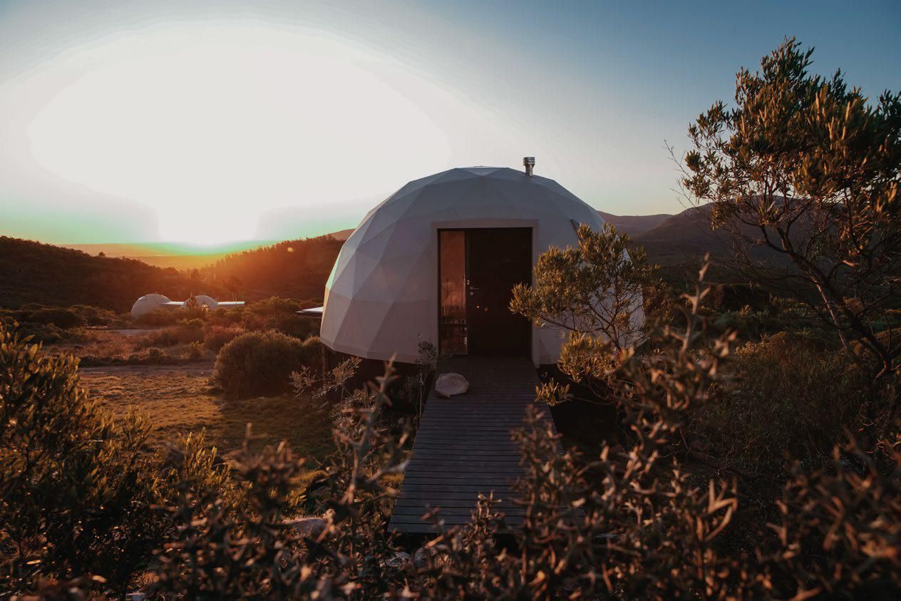 Una tienda de campaña tipo cúpula está situada en medio de un campo al atardecer.