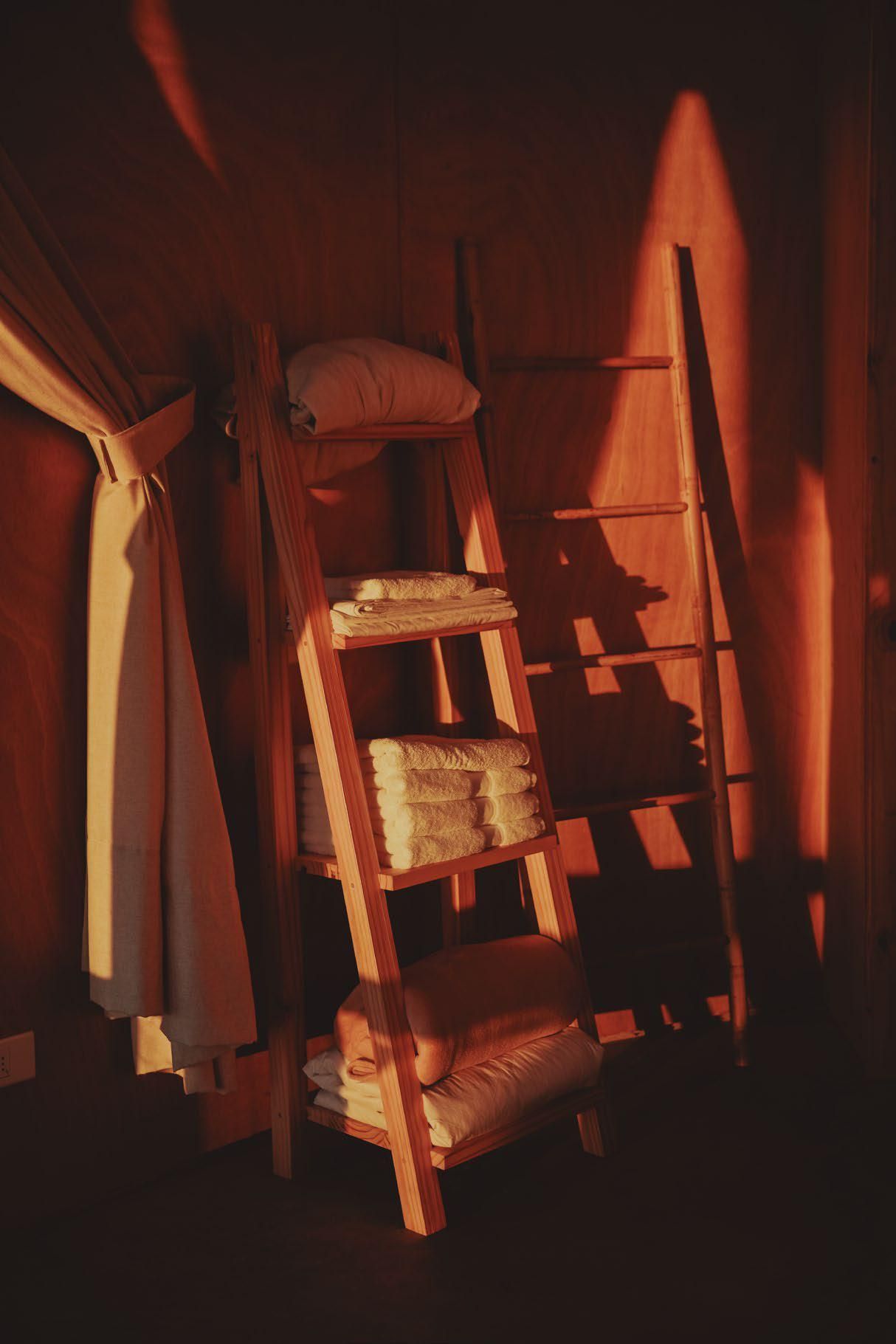 Hay una escalera de madera junto a un estante con toallas.