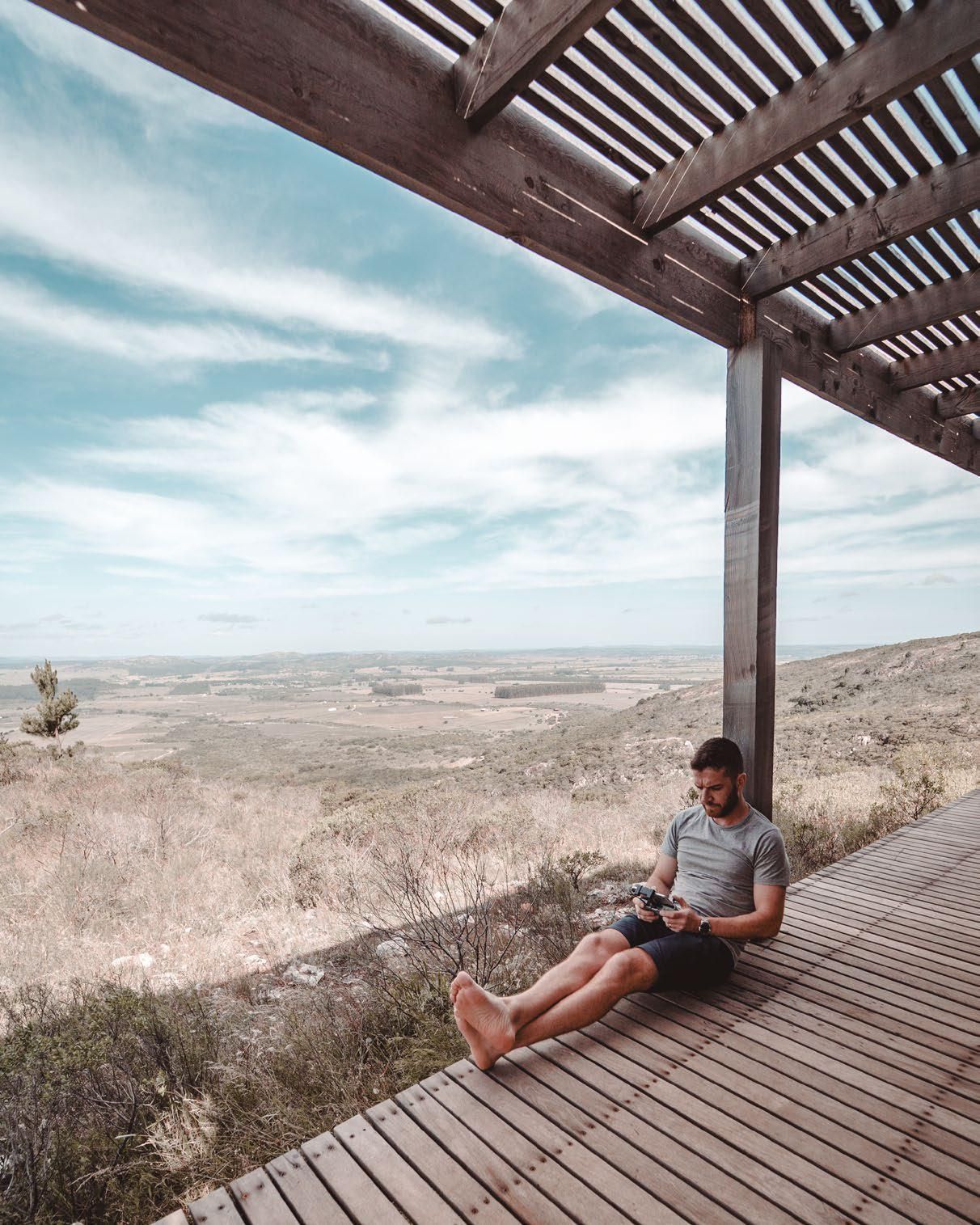 Un hombre está sentado en una terraza de madera leyendo un libro.
