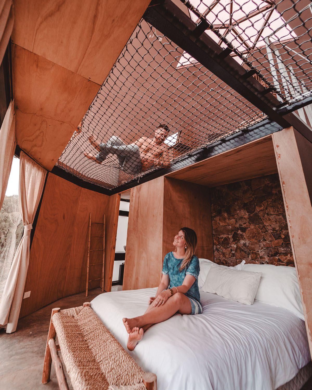 Una mujer está sentada en una cama en una habitación con un hombre tendido en el techo.