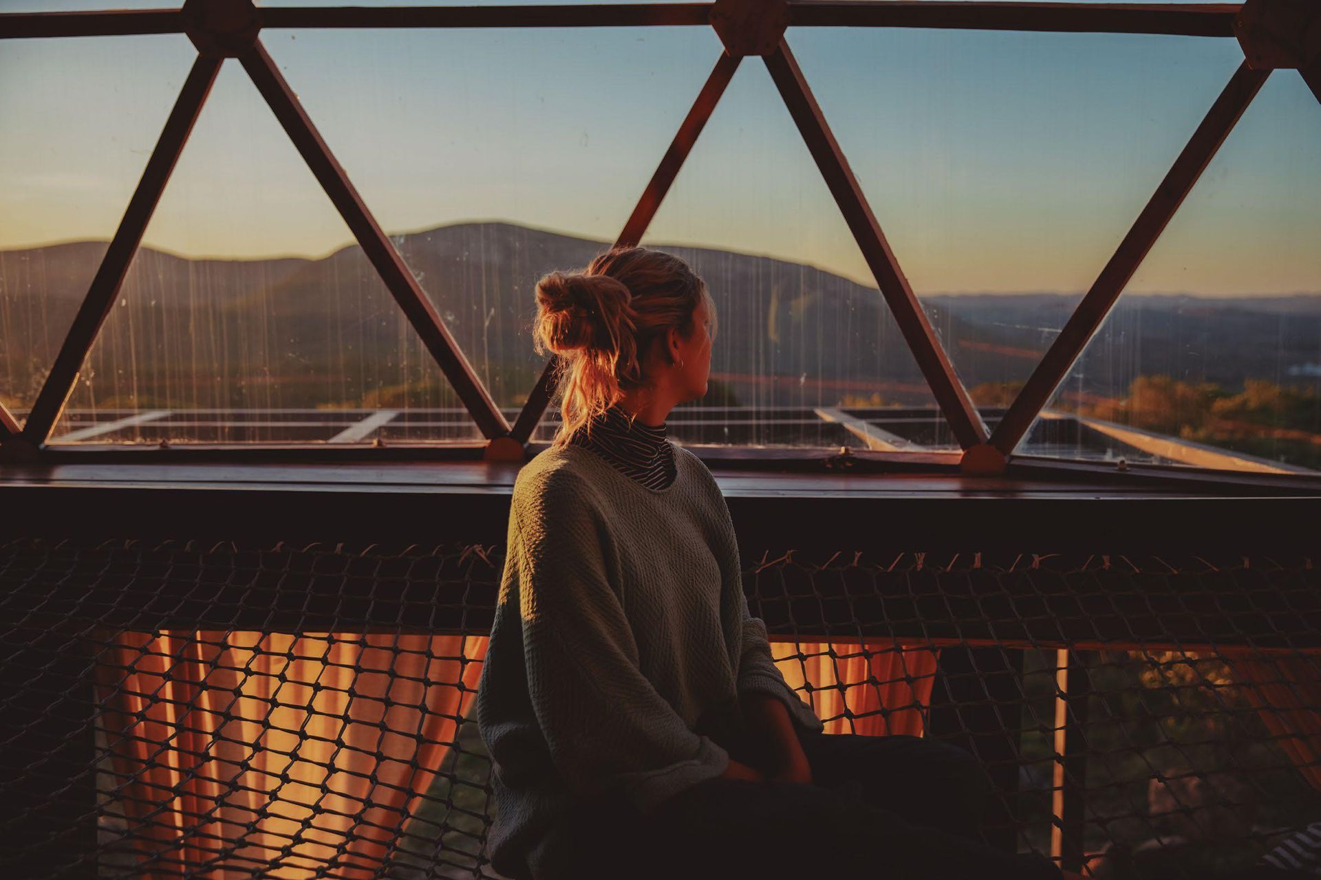 Una mujer está sentada en un balcón mirando por una ventana al atardecer.