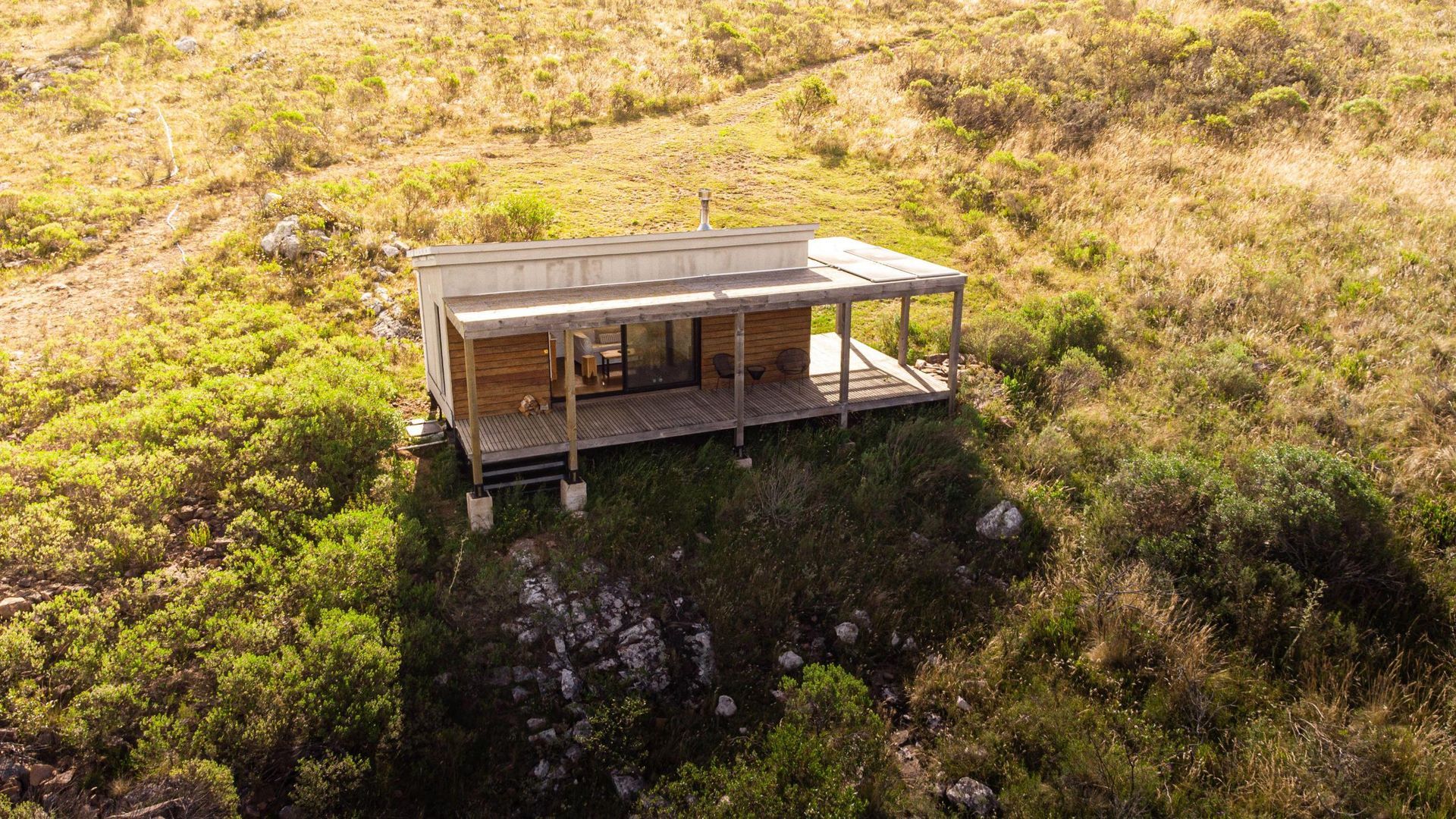 Una vista aérea de una pequeña casa en la cima de una colina rodeada de árboles.
