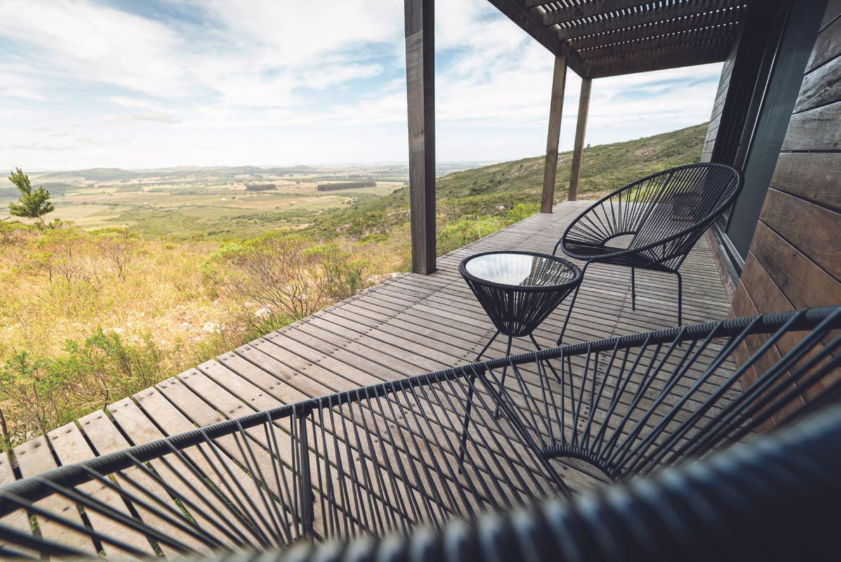 Un deck de madera con sillas y una mesa con vista a un campo.