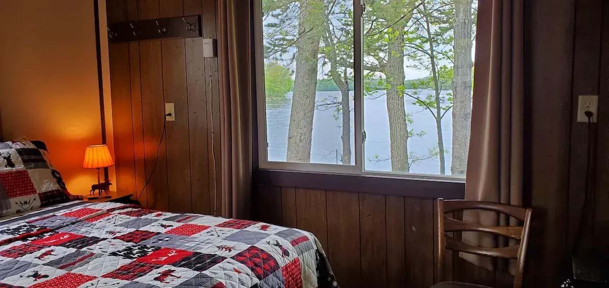 Cozy bedroom with red-and-black quilt, bedside lamp, and a window overlooking trees and water