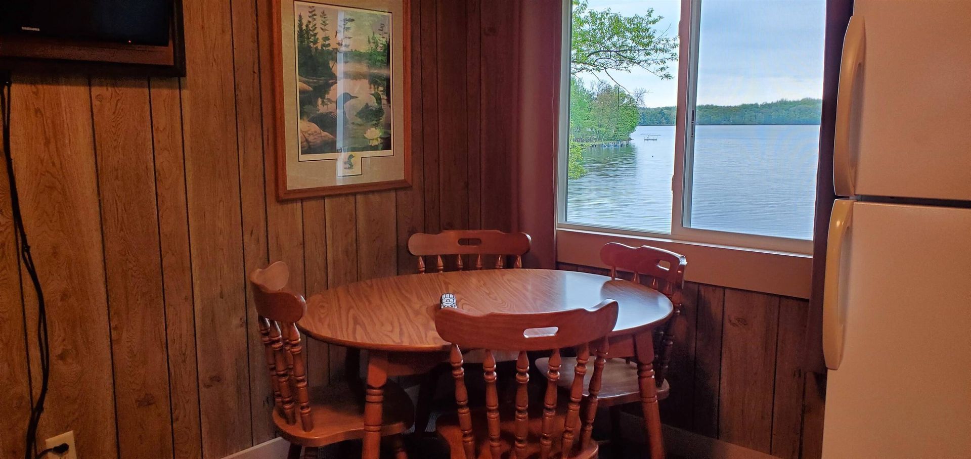 Wood-paneled cabin dining nook with round table, chairs, and a lake view through the window.