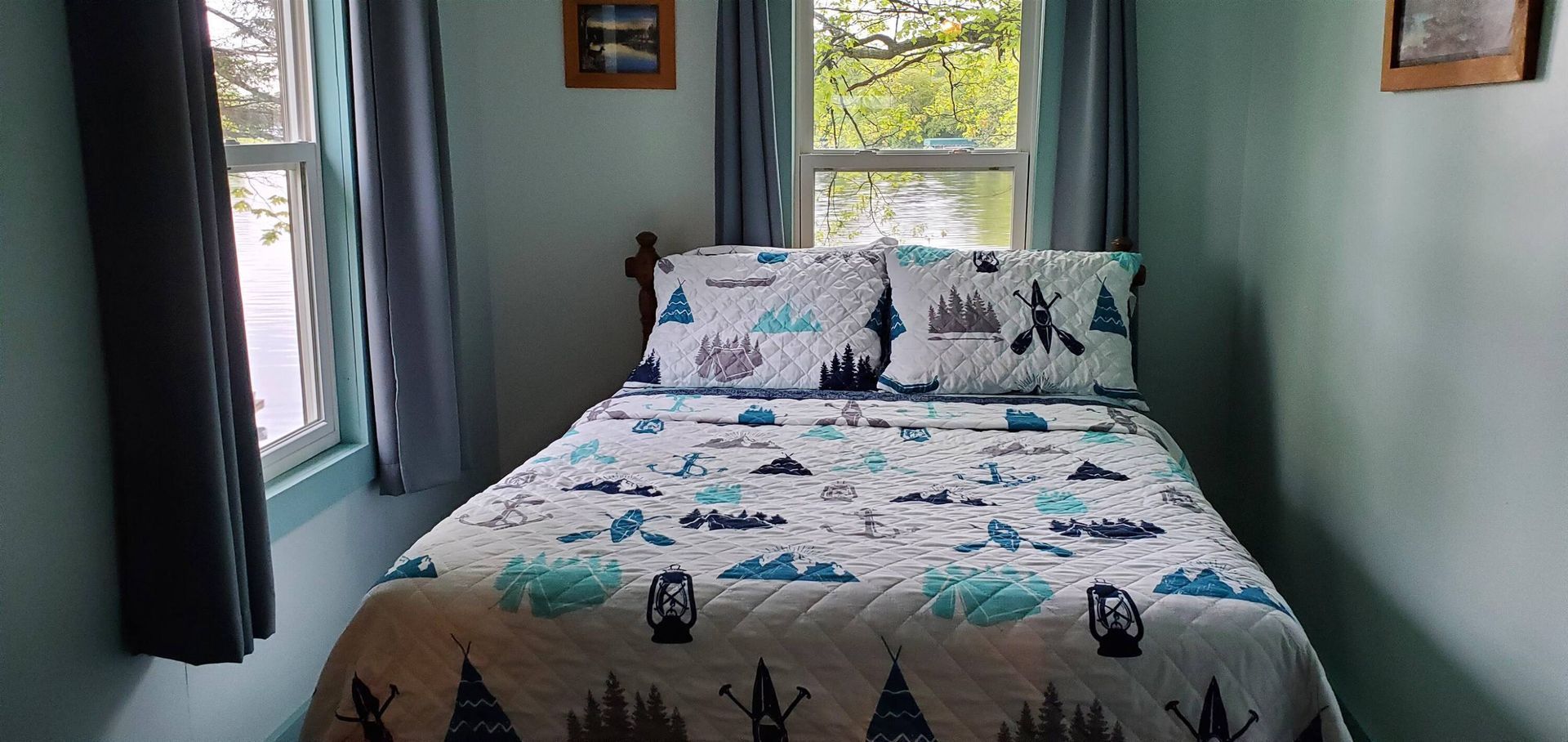 Neatly made bed with white cat-patterned bedding in a small teal bedroom by a window