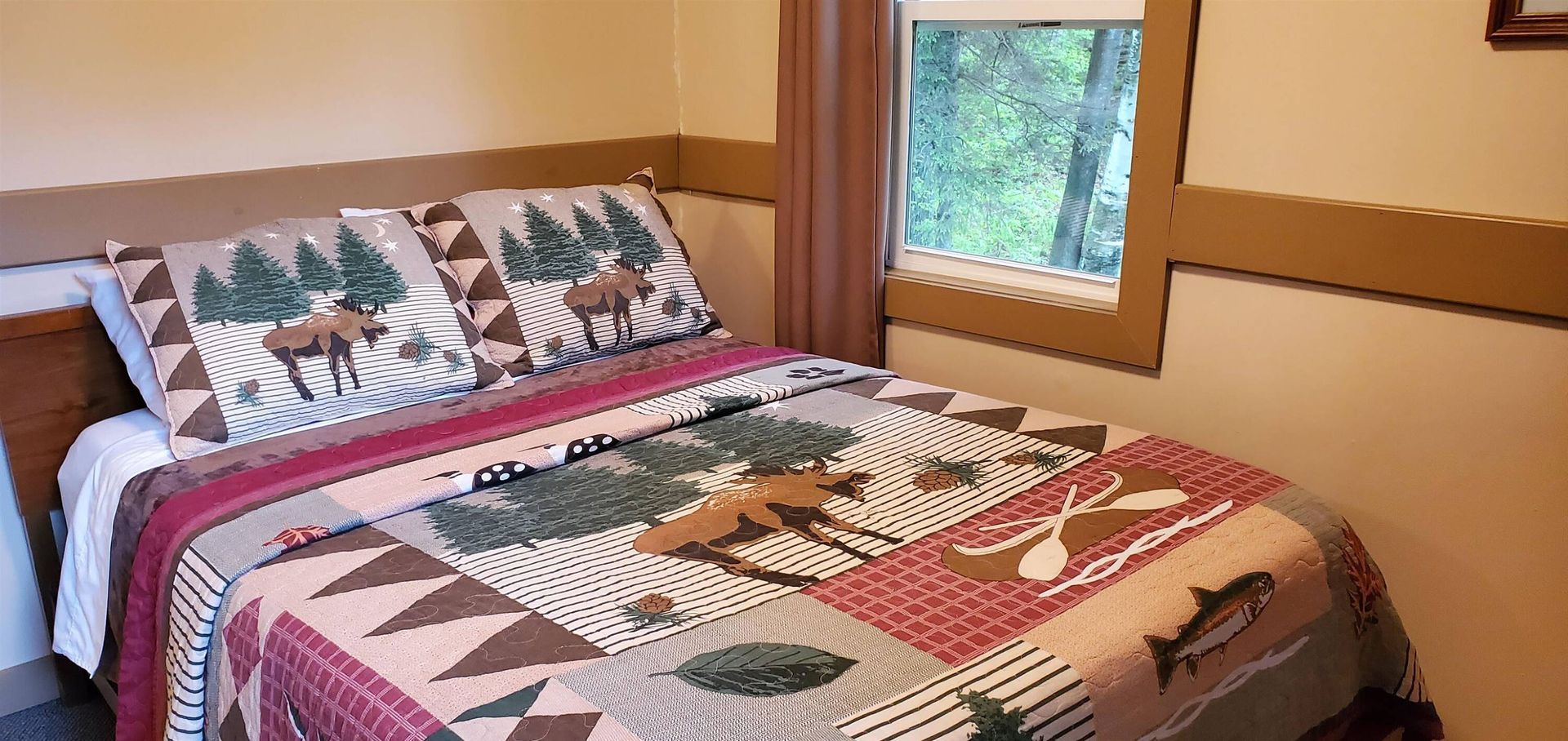 Colorful bed with leaf-patterned bedding in a small bedroom beside a window overlooking greenery