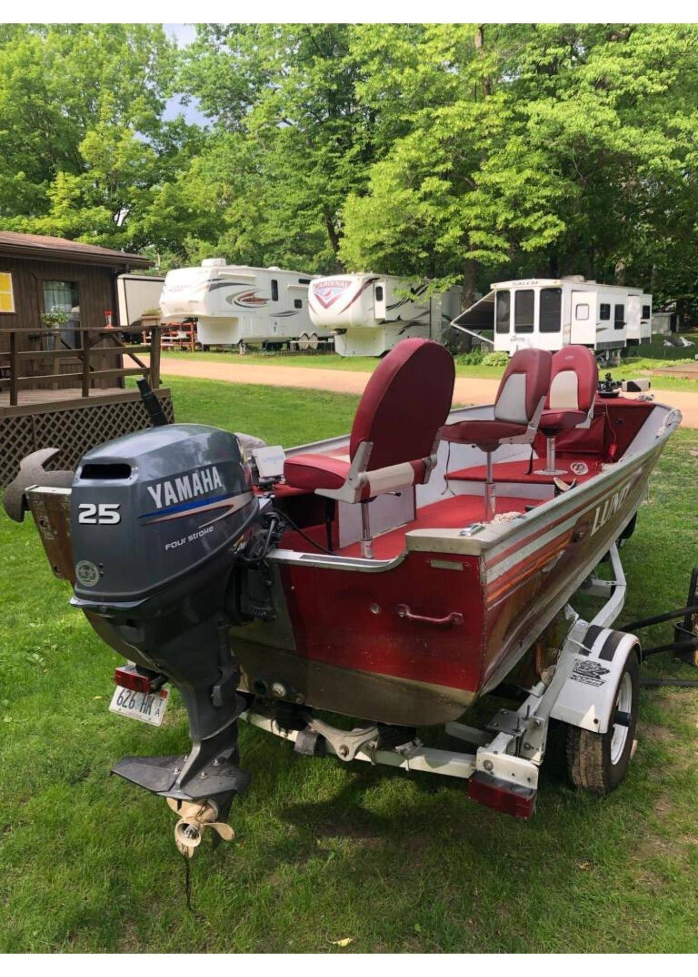 Red fishing boat on a trailer with a black Yamaha outboard, parked on grass near RVs.