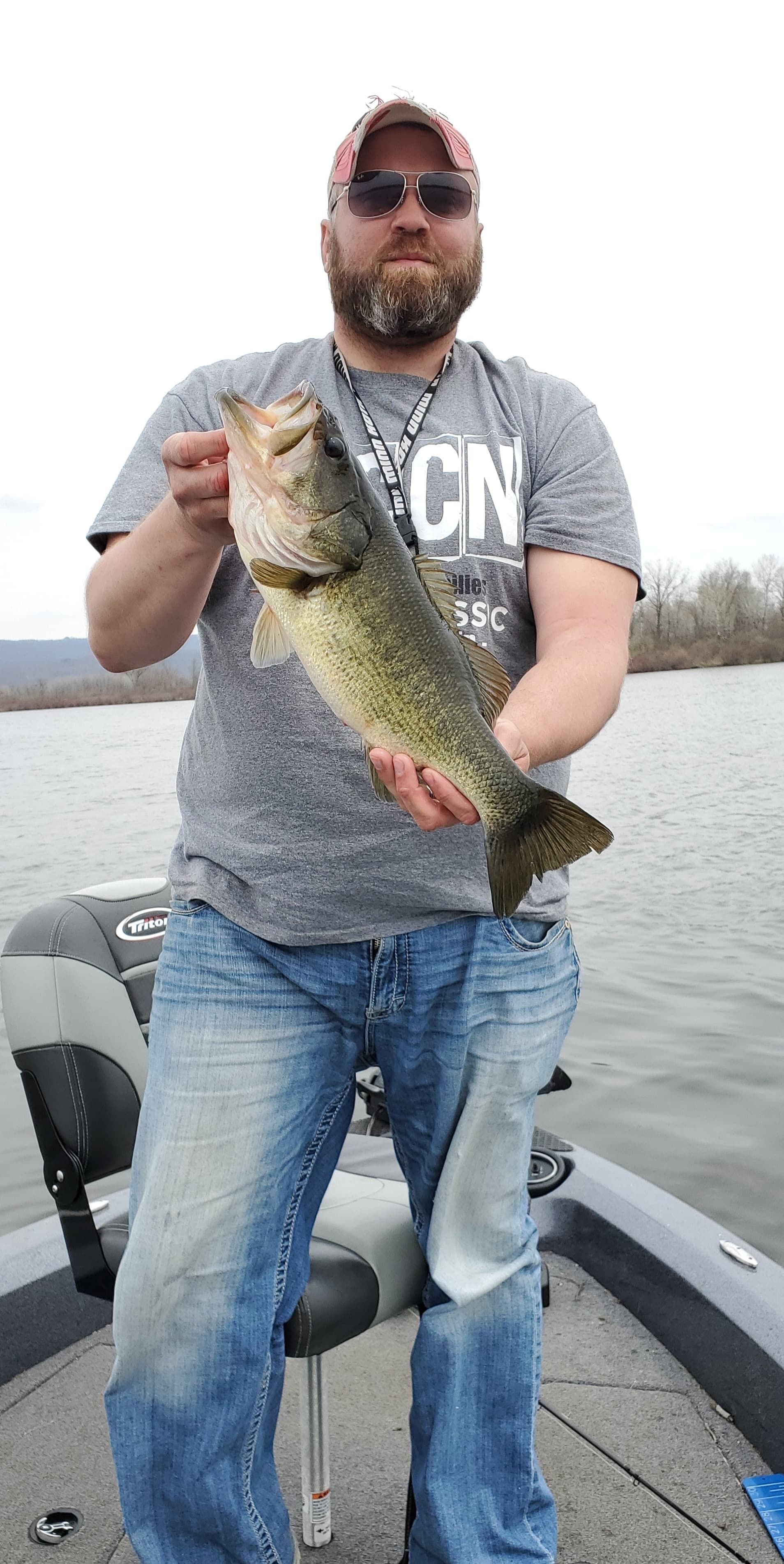 Angler on a boat holding a large fish by the lake