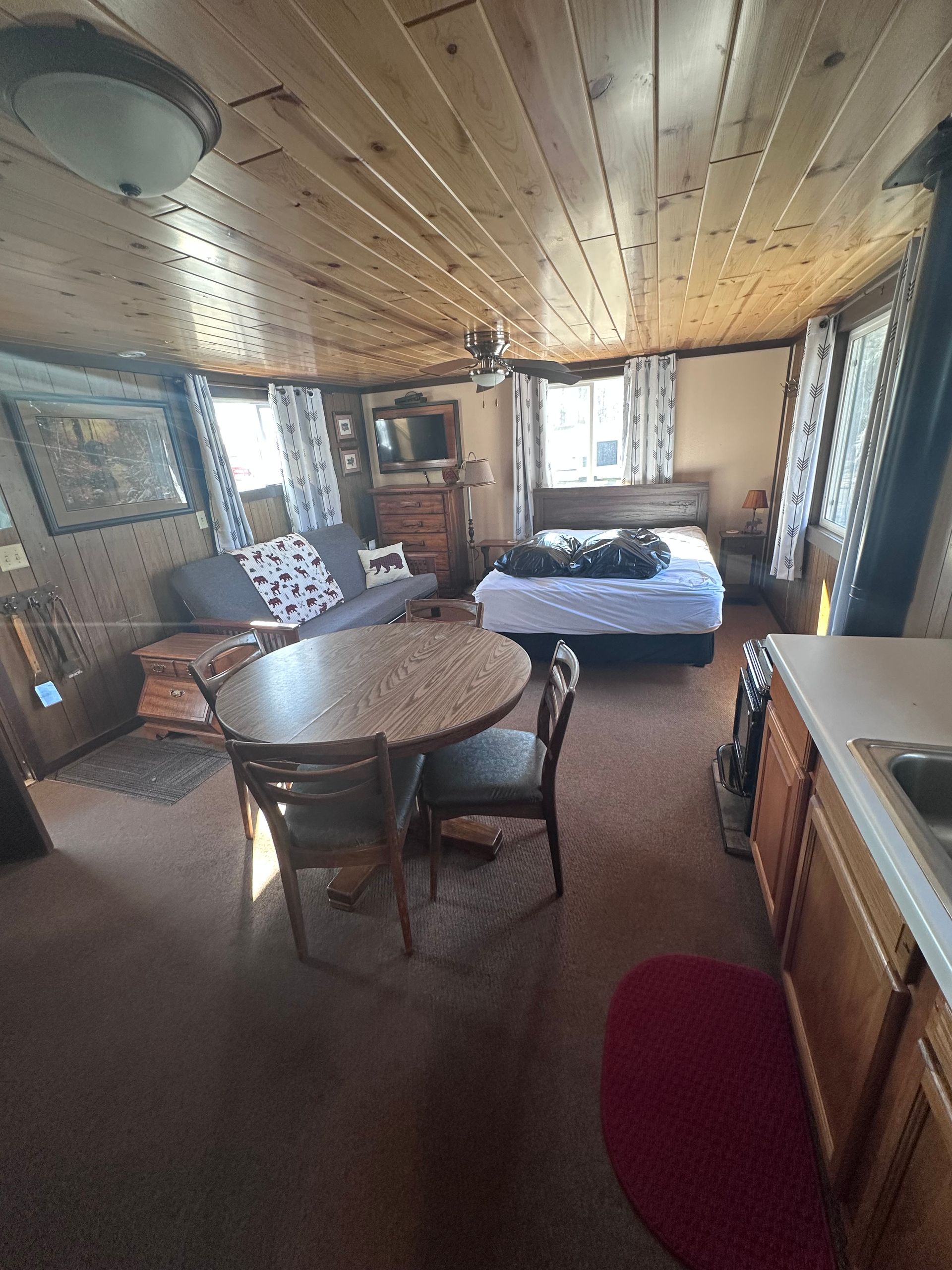 Cozy cabin bedroom with wood-paneled walls, round table, twin beds, and a window view outside