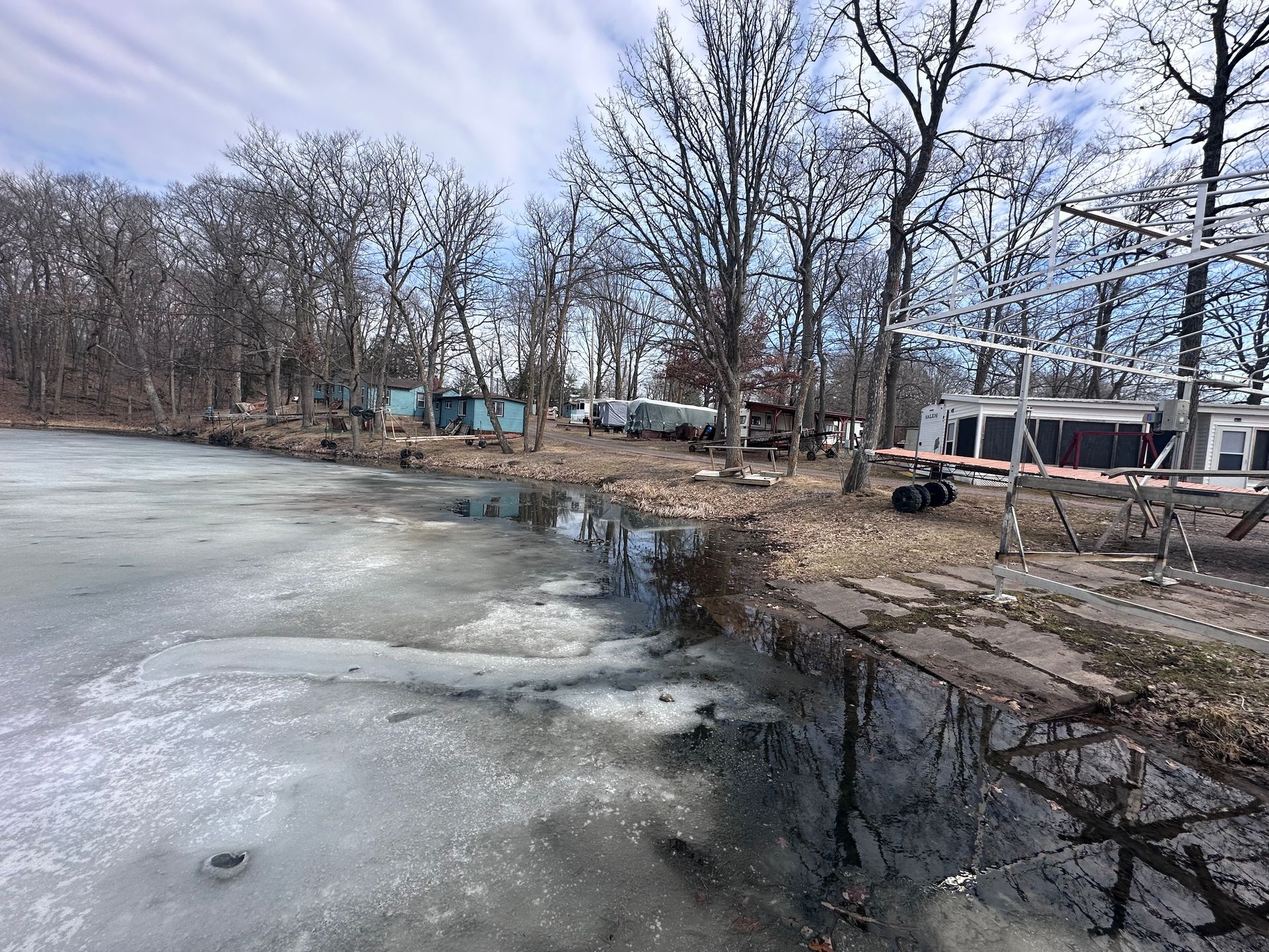 Frozen pond beside leafless trees and a dock on a cloudy winter day
