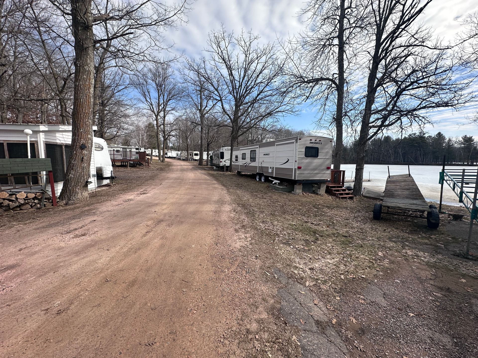 Dirt road beside parked RVs and trailers near a lakeshore in a wooded campground