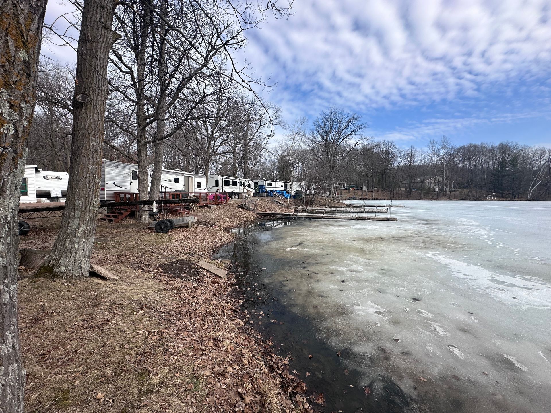 Frozen lakeshore with leafless trees and parked RVs on a cloudy winter day