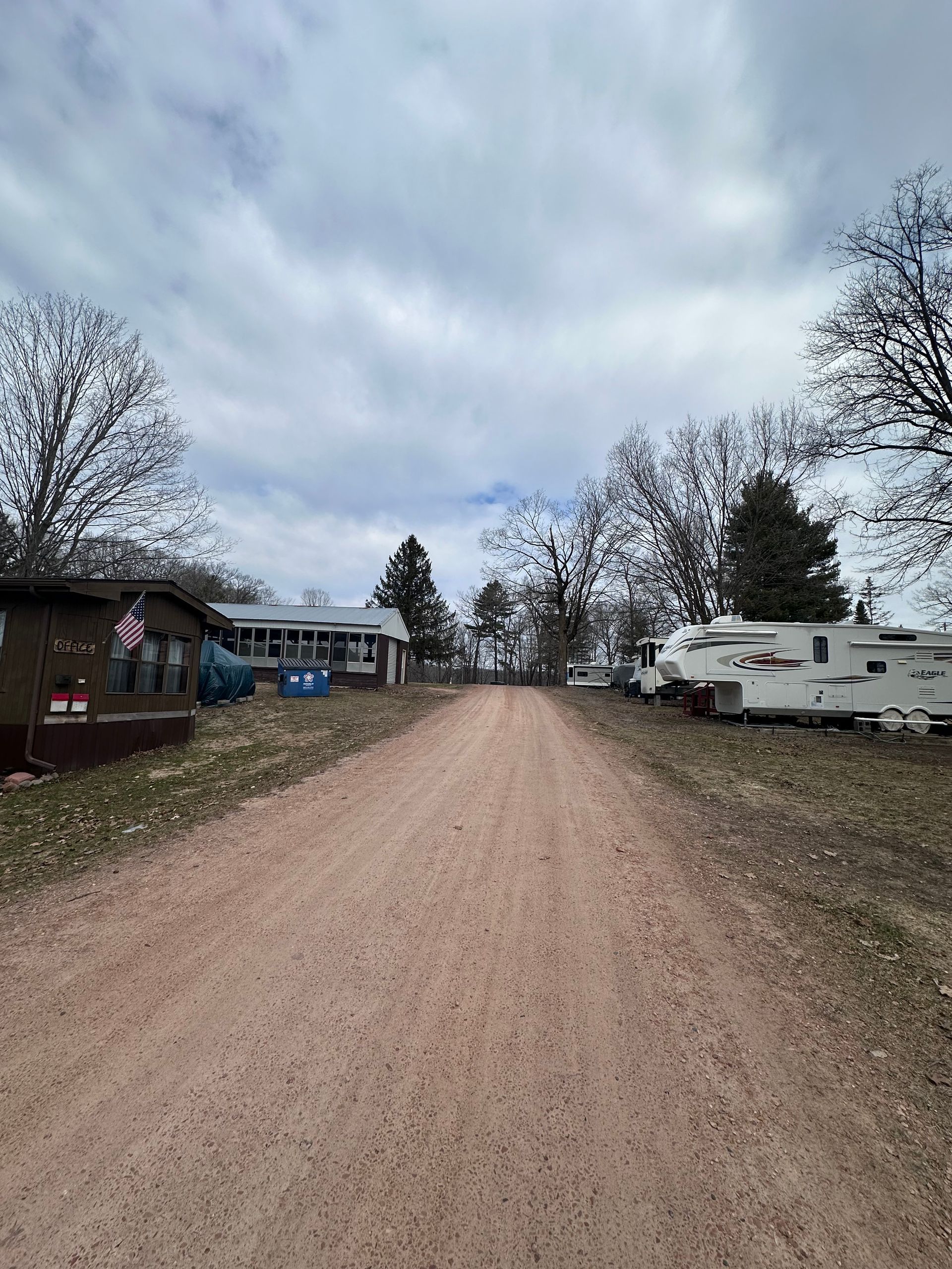 Gravel road in a campground with RVs and leafless trees under a cloudy sky
