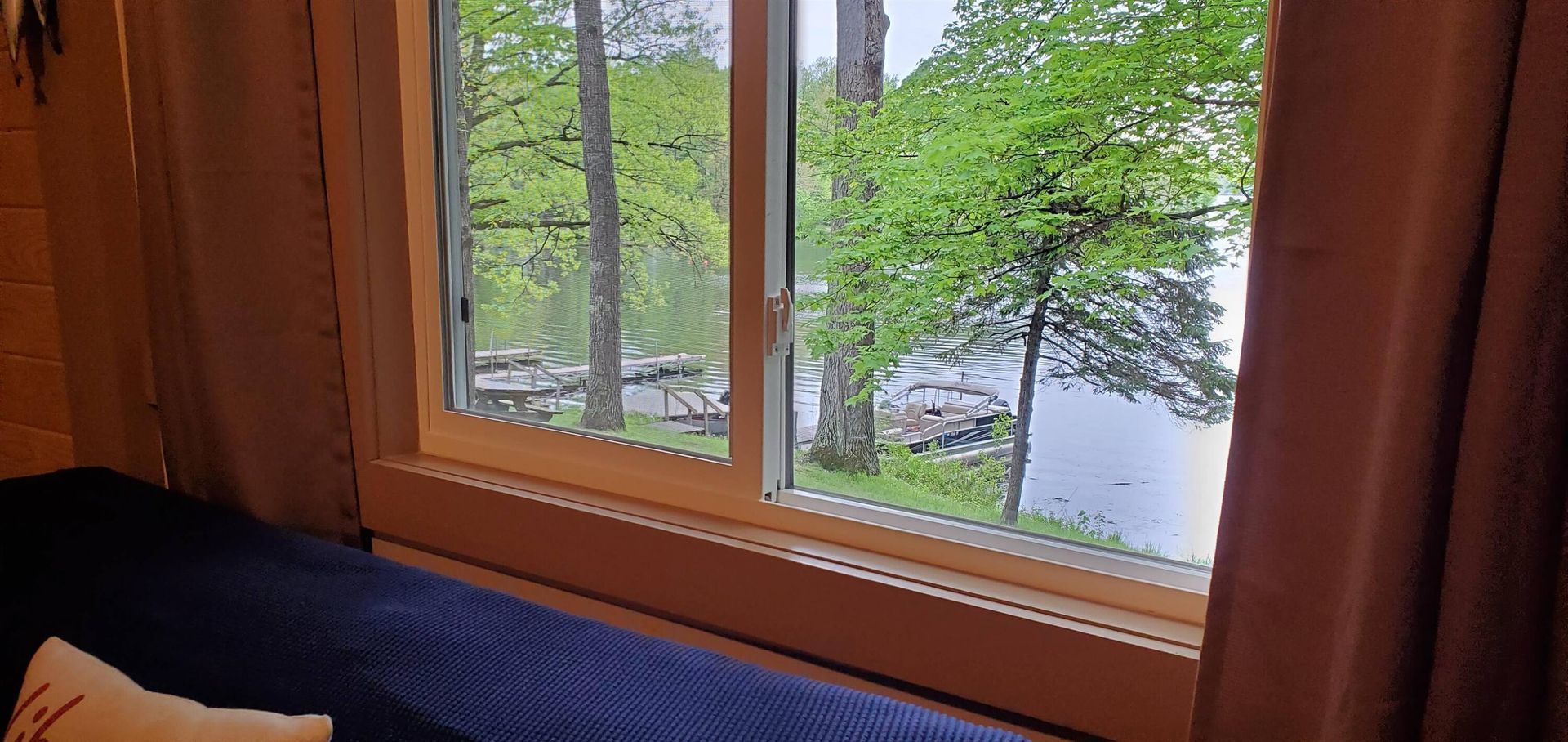 Cozy room with blue bed, wooden window frame, and green trees visible outside