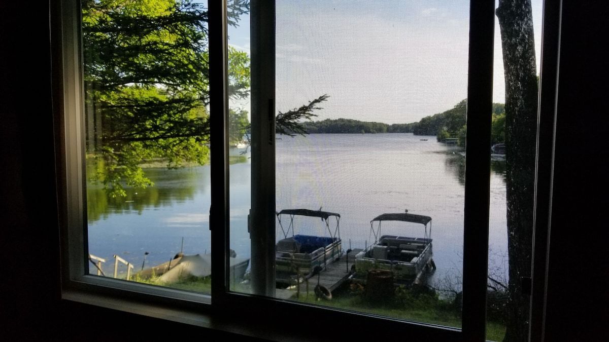 Lakeside view through a window with boats docked by a calm lake and trees along the shore