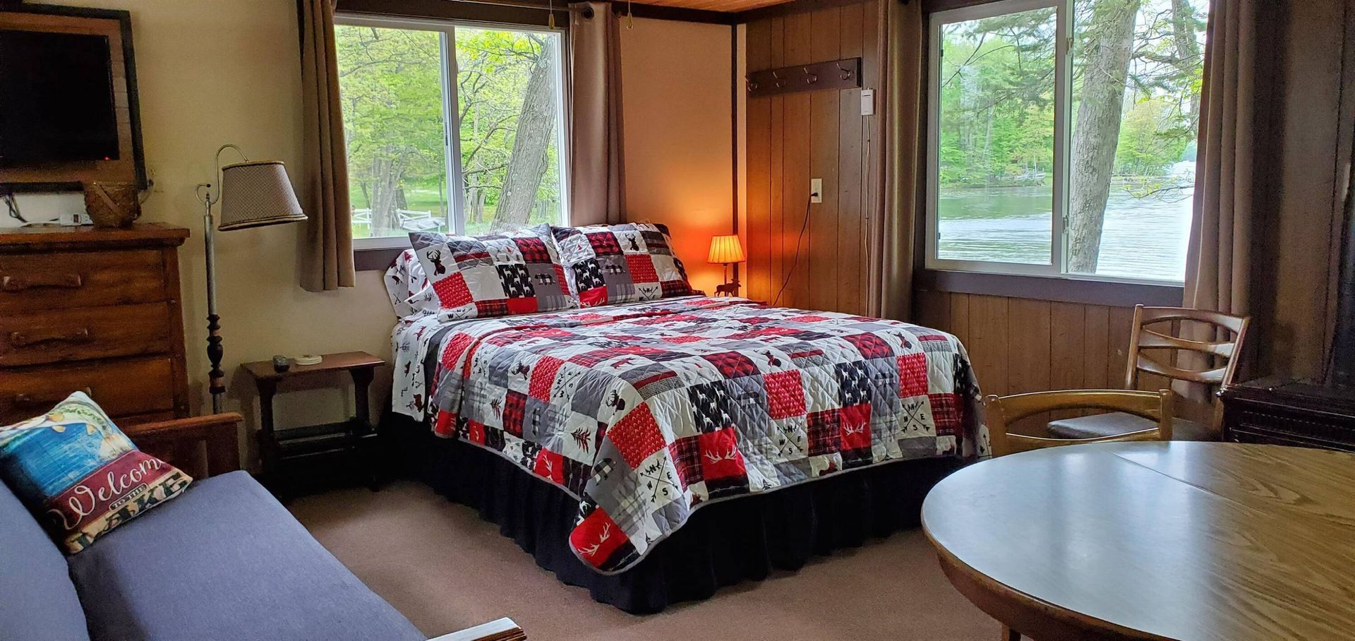 Cozy bedroom with a patterned bedspread, wooden walls, and large windows overlooking trees