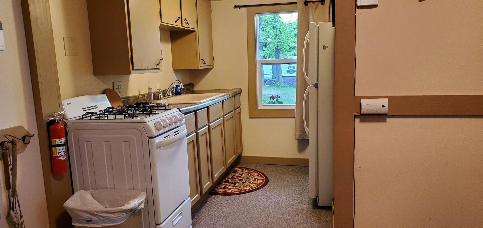 Narrow kitchen with beige cabinets, white stove and fridge, and a window at the end.