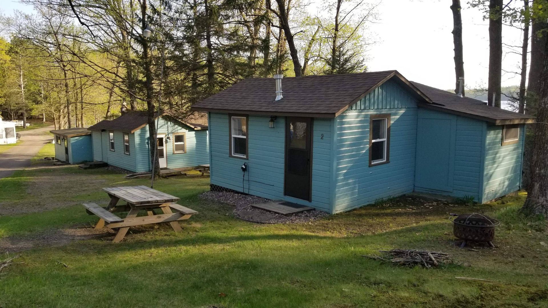 Blue cabins in a wooded campsite with a picnic table and a fire pit in the foreground.