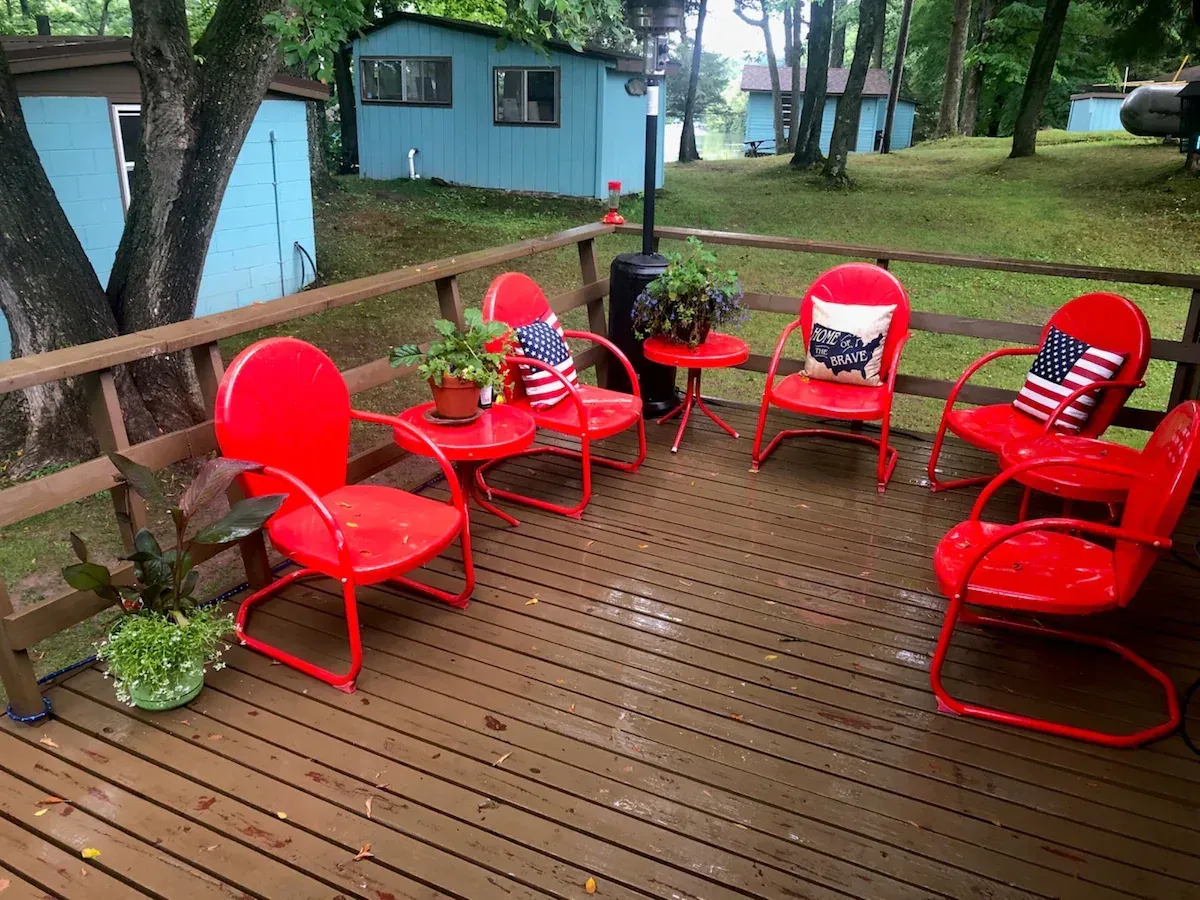 Red outdoor chairs arranged on a wooden deck beside a blue house and trees