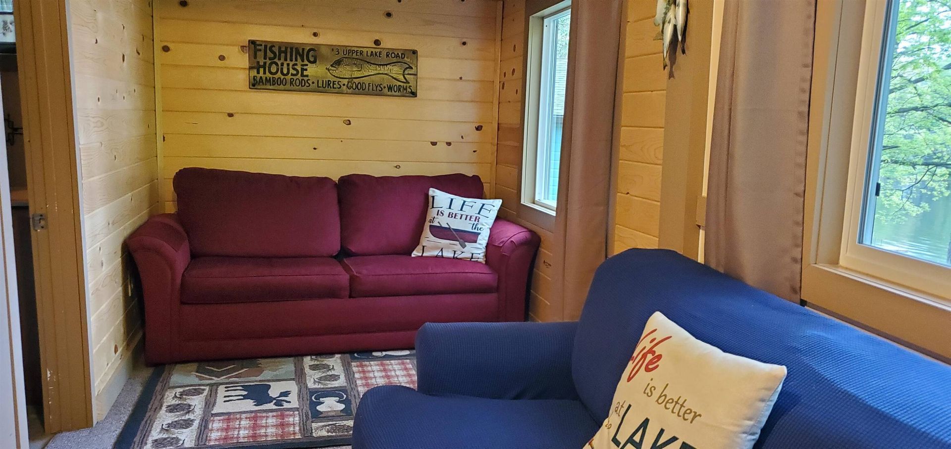 Cozy log cabin living room with red and blue sofas, patterned rug, and wood-paneled walls.