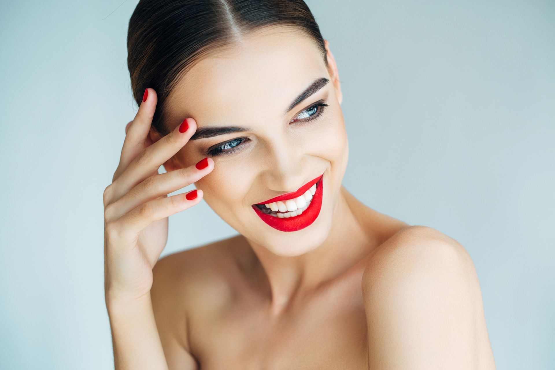 A woman with red lipstick and red nails is smiling.