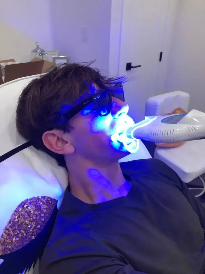 A man wearing sunglasses is getting a teeth whitening treatment.