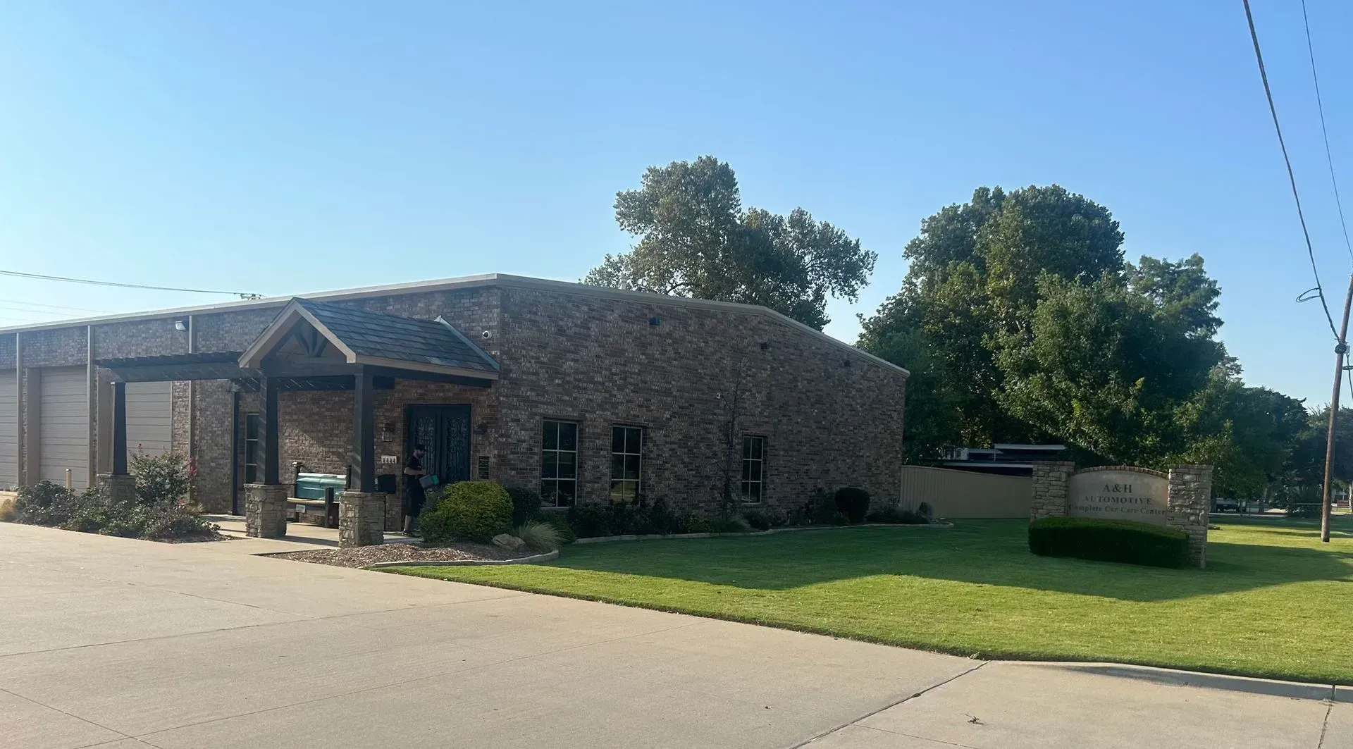 Brick building with a covered entrance, two garage doors, and green lawn. Clear blue sky. | A&H Automotive Repair Shop