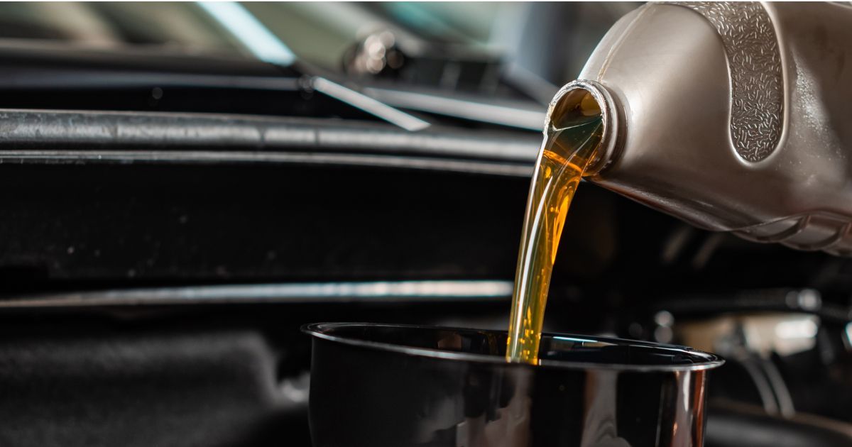 Motor oil pouring from a container into a black receptacle, set in an engine bay.