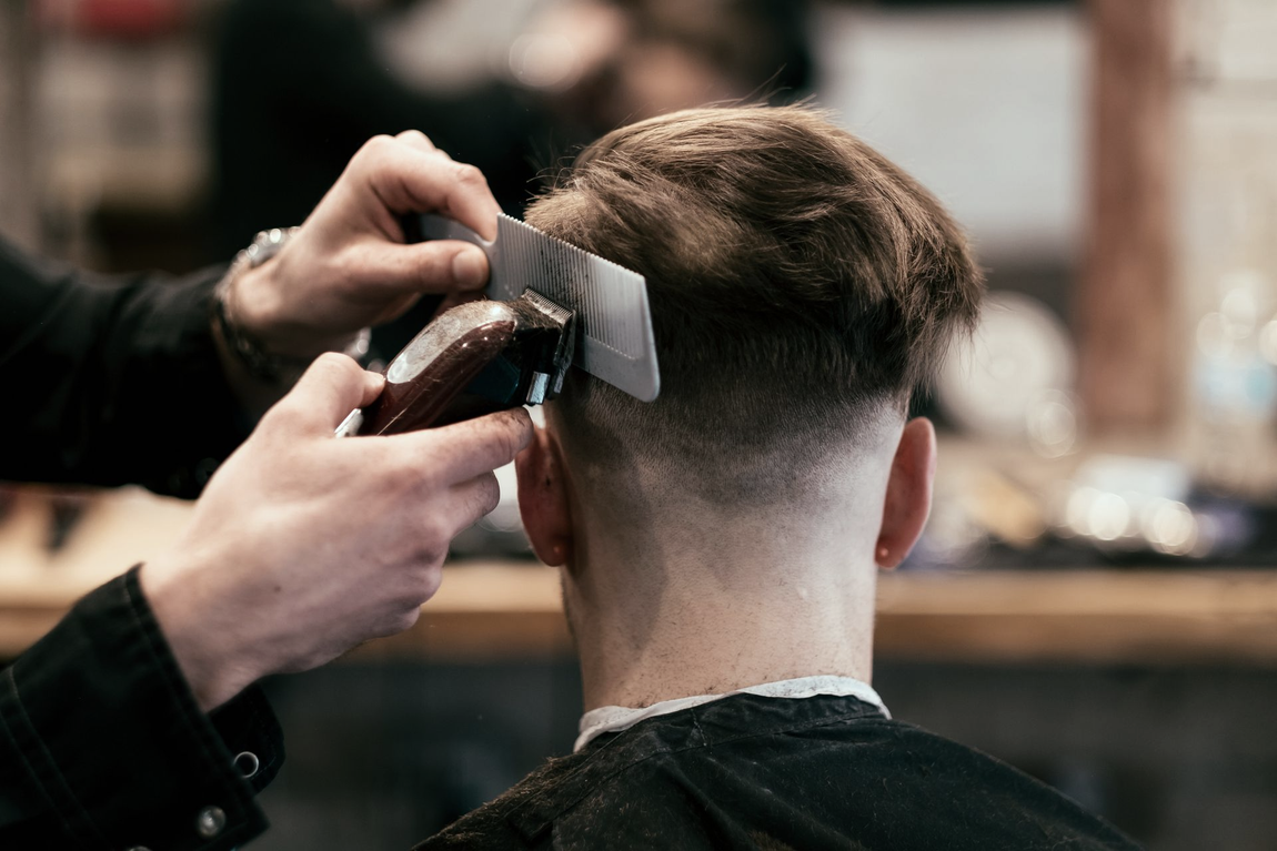 Un barbiere utilizza un tagliacapelli con protezione per tagliare i capelli di un cliente, creando una sfumatura.