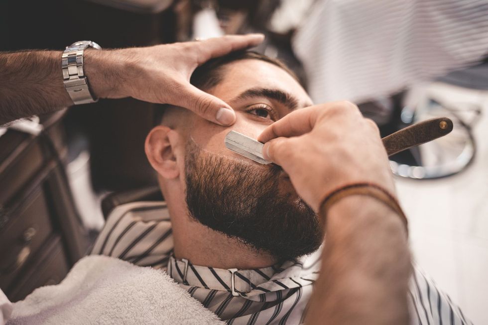 Un barbiere rade il viso di un uomo con un rasoio a mano libera in una bottega da barbiere.
