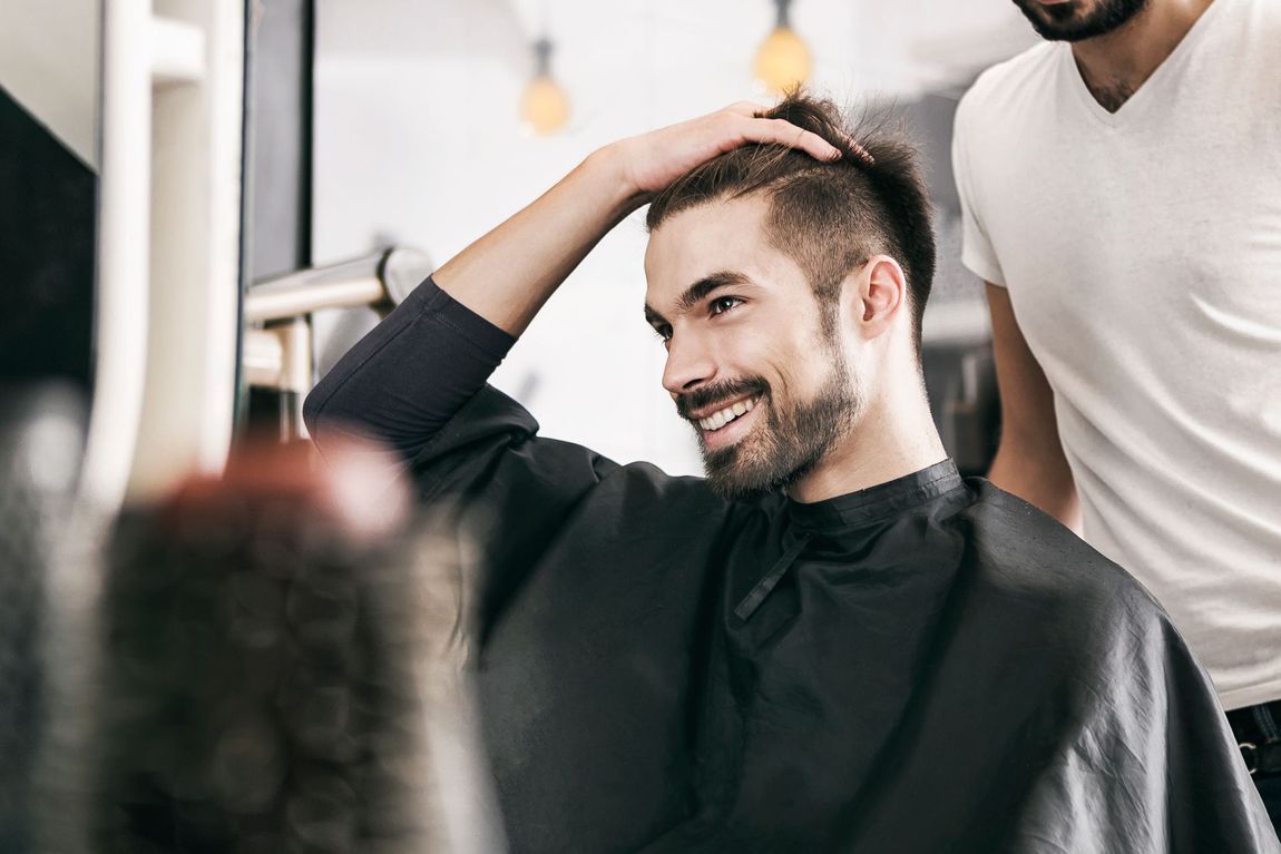 Un uomo sorride al suo nuovo taglio di capelli in un salone. Il barbiere è in piedi dietro di lui, ed entrambi gli guardano i capelli.