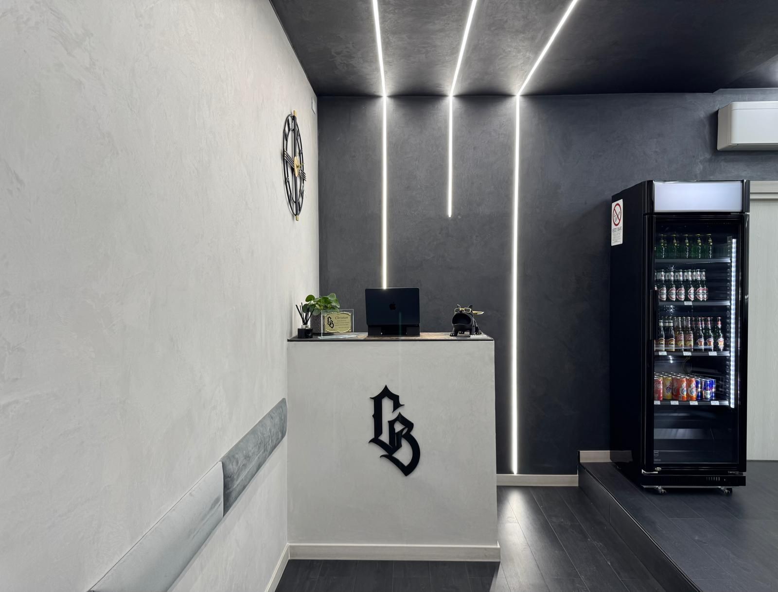 Reception di uno studio di tatuaggi, arredamento in bianco e nero, con frigorifero e orologio.