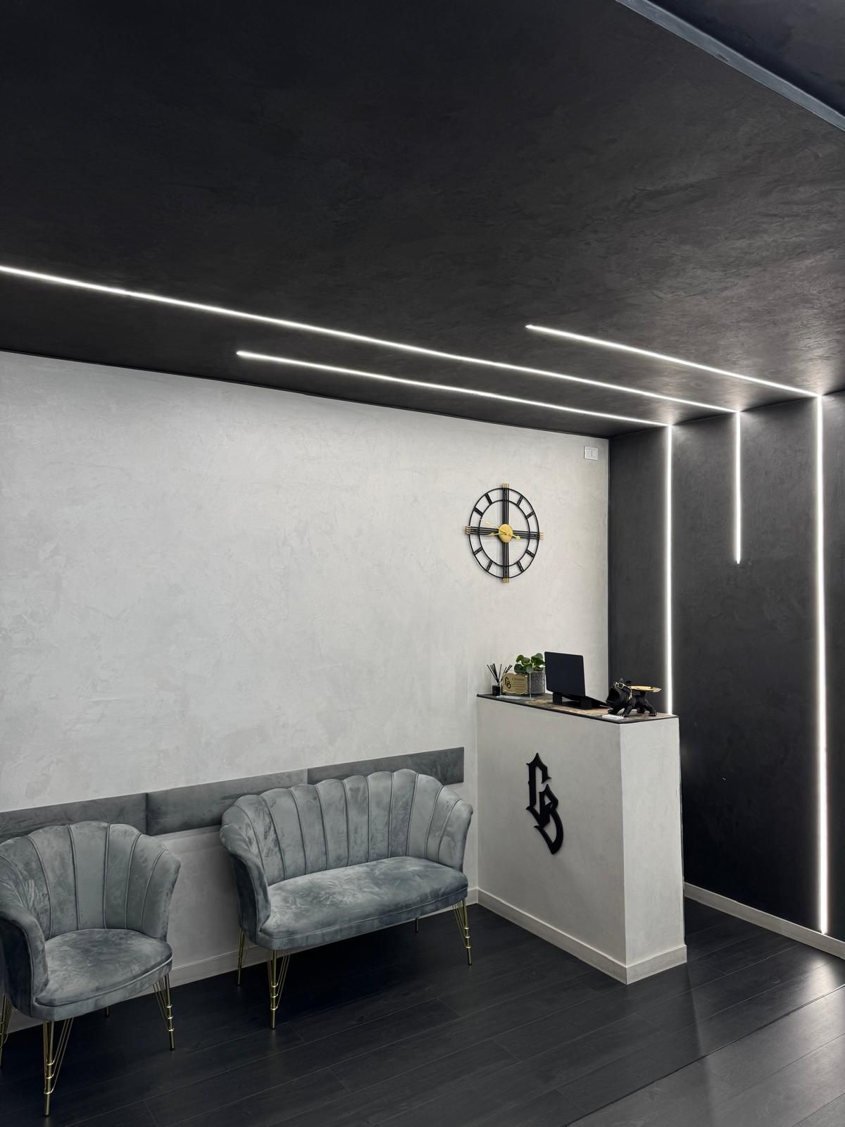 Una moderna area reception con decorazioni grigie e bianche, sedute in velluto e illuminazione lineare.