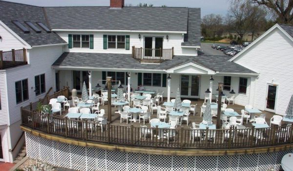 A large white house with tables and chairs on the deck