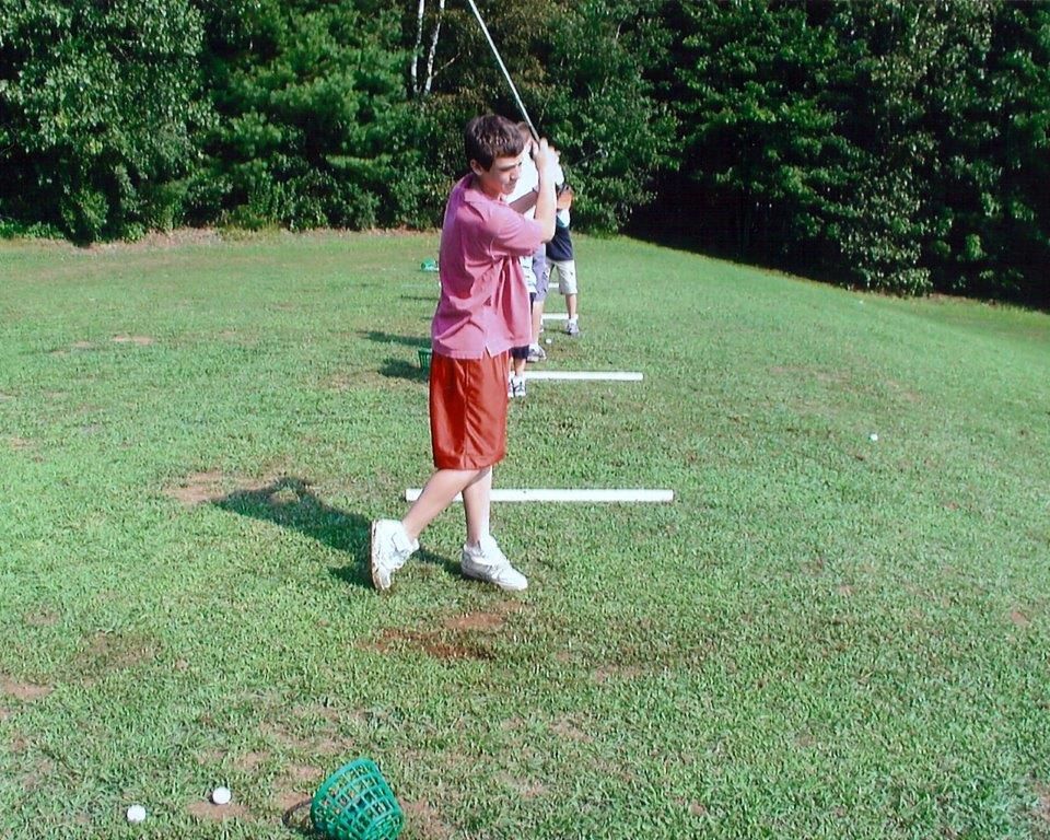 A boy in a pink shirt is swinging a golf club