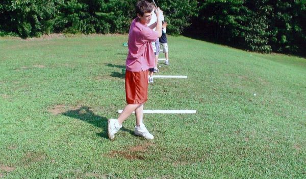 A boy in a pink shirt and red shorts is swinging a golf club.