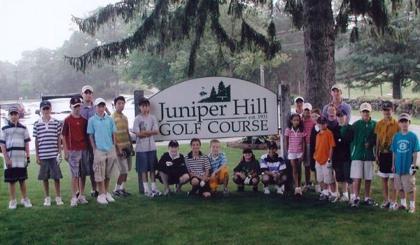 A group of people standing in front of a juniper hill golf course sign