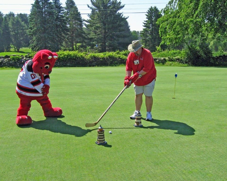 A man and a mascot are playing golf on a green